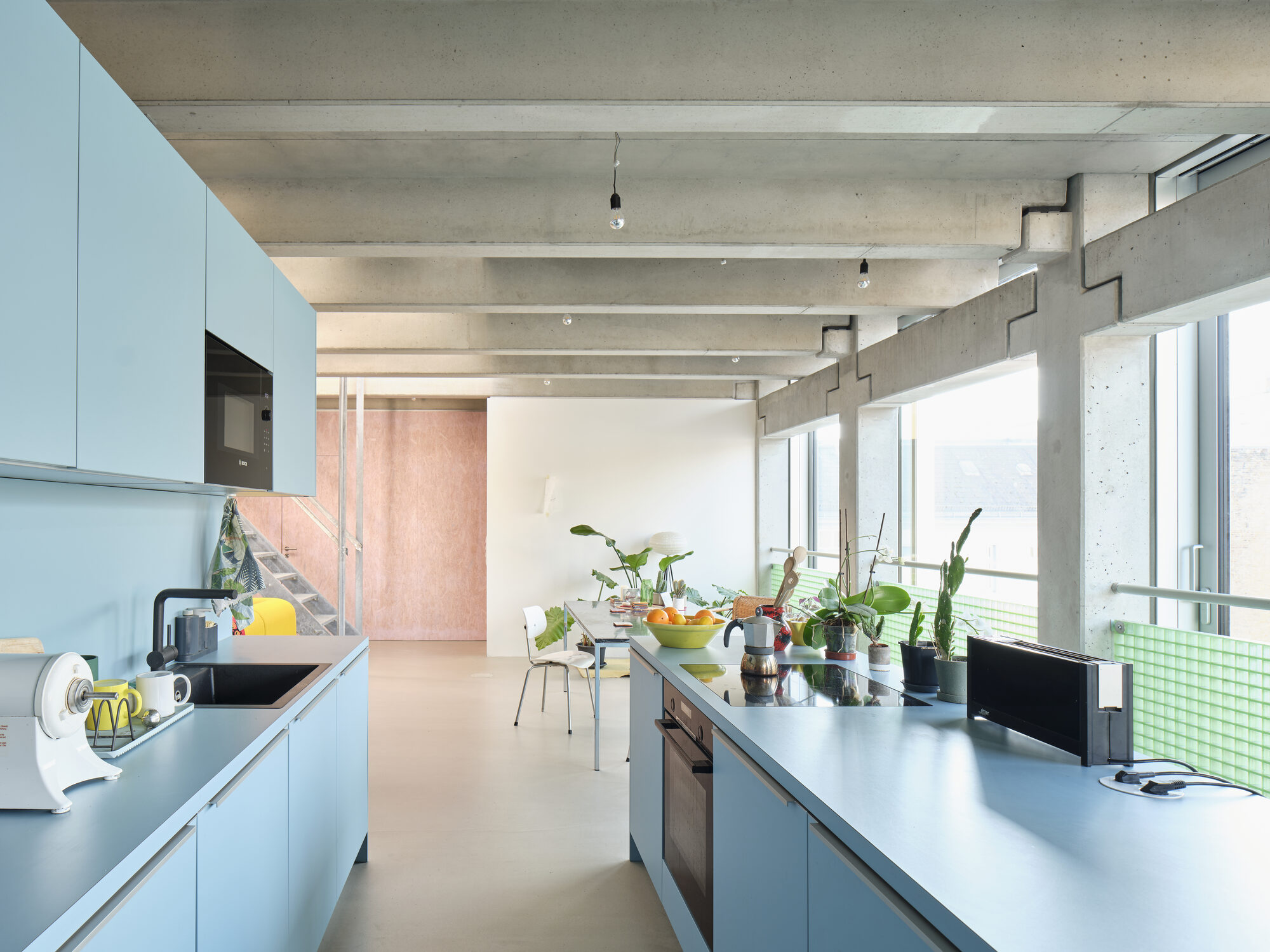 Wohnregal live-work atelier interior with blue kitchen cabinetry, exposed concrete beams, and large windows