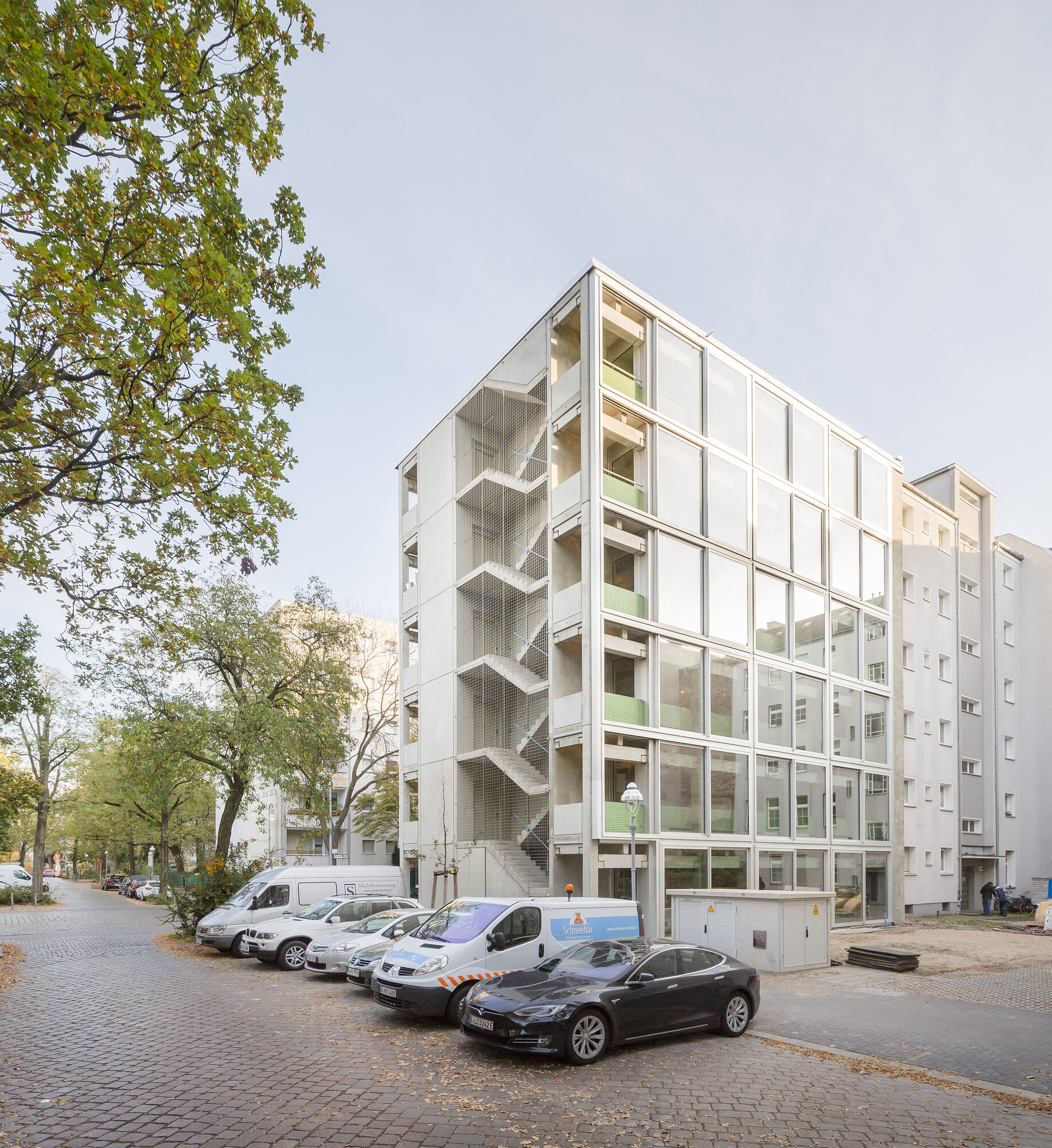 Wohnregal exterior with a precast concrete frame, glass facade, and green balcony panels on a Berlin street corner