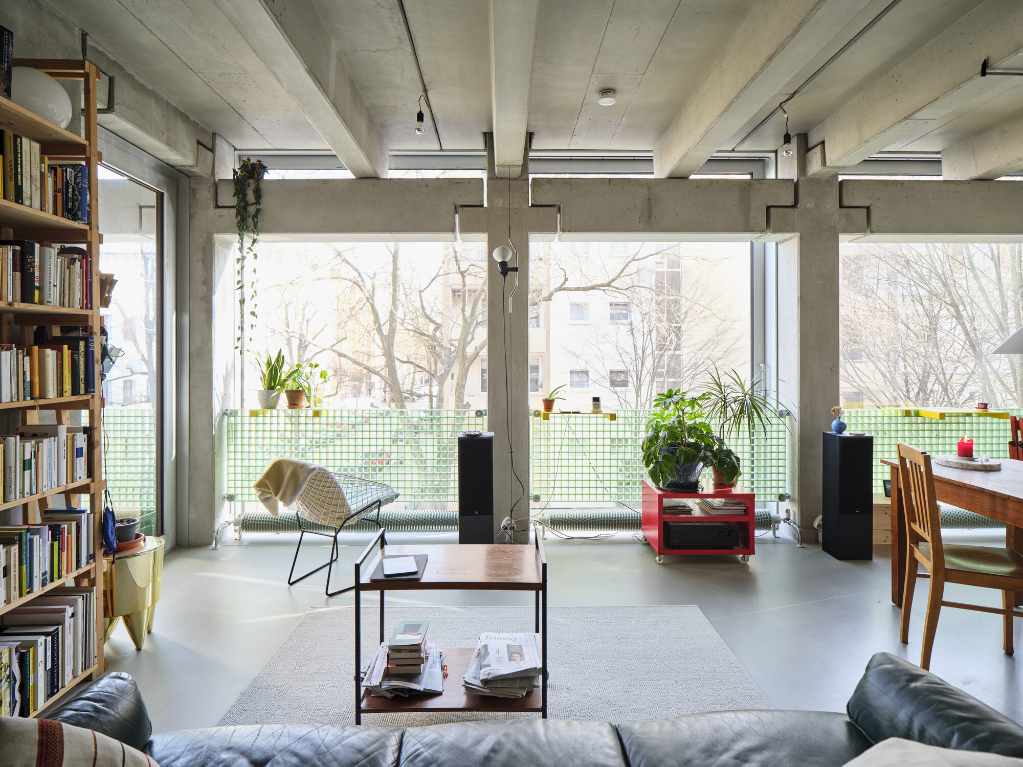 Furnished Wohnregal live-work interior with exposed concrete beams, dining area, and large sliding glass facade